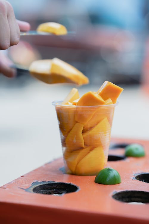 A person is cutting up mangoes into a cup
