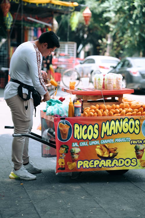 A man is standing next to a cart selling mangoes