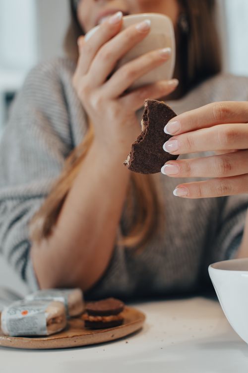 Free A woman sipping coffee and holding a partially eaten chocolate cookie indoors. Stock Photo