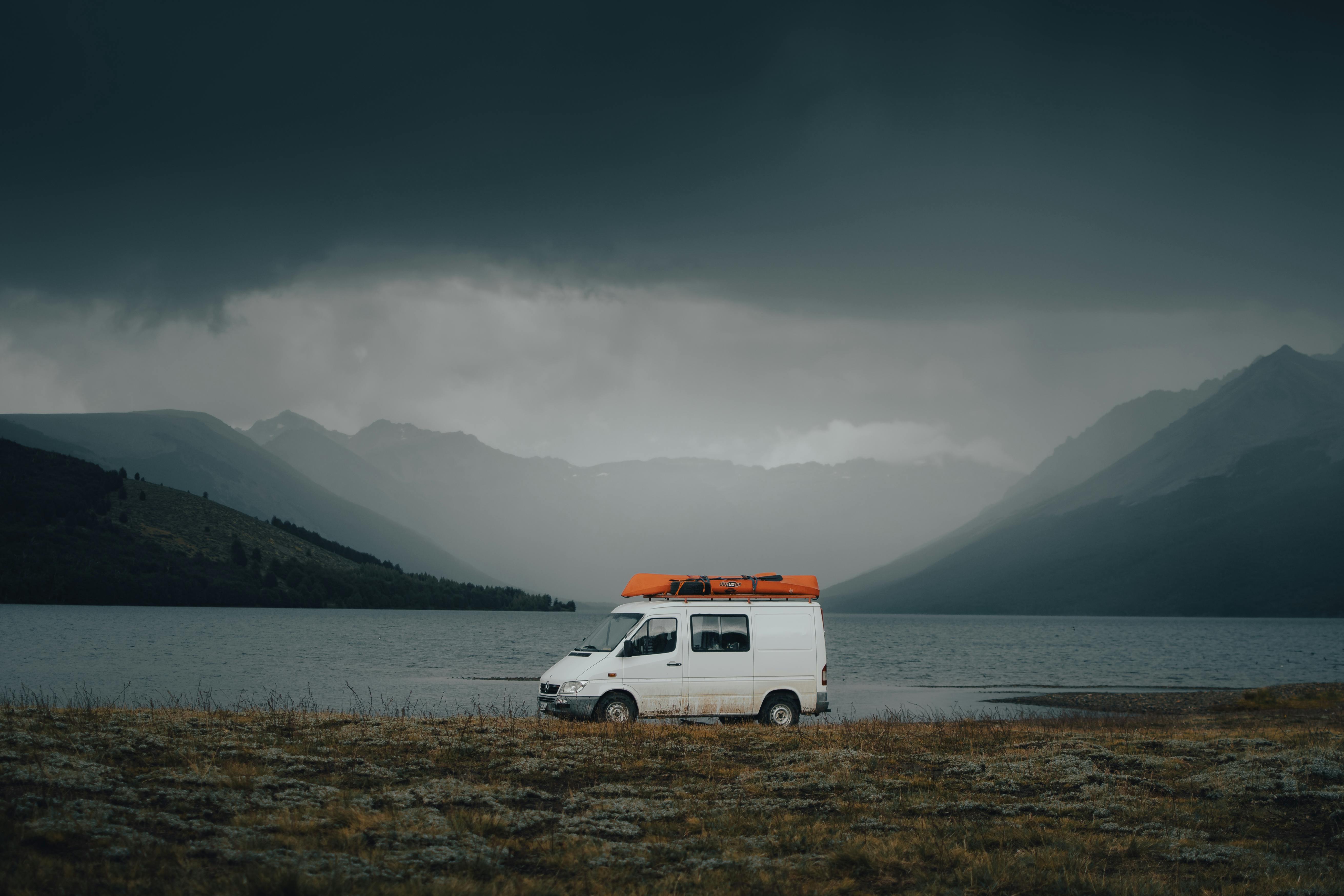 White campervan parked by a misty mountain lake under dramatic cloudy skies, perfect for travel adventures.