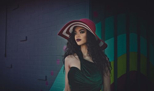 Free Stylish woman in a red hat standing against a colorful urban wall, embodying modern fashion. Stock Photo