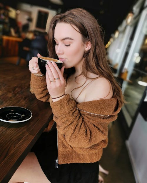 Selective Focus Photo of Woman Sitting at Table in Coffee Shop Sipping Coffee