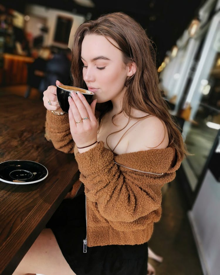 Selective Focus Photo Of Woman Sitting At Table In Coffee Shop Sipping Coffee