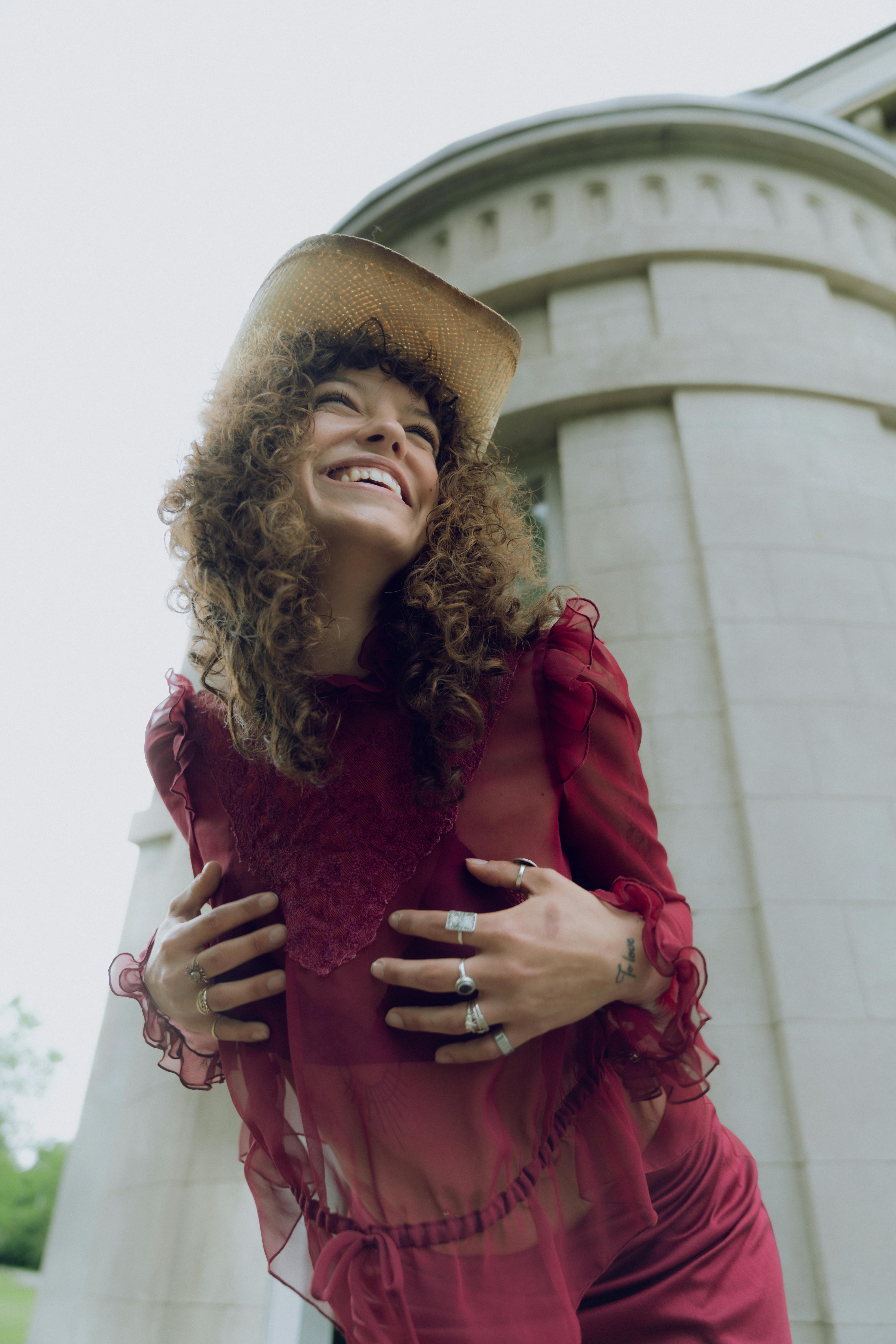 A woman in a red dress and hat is smiling