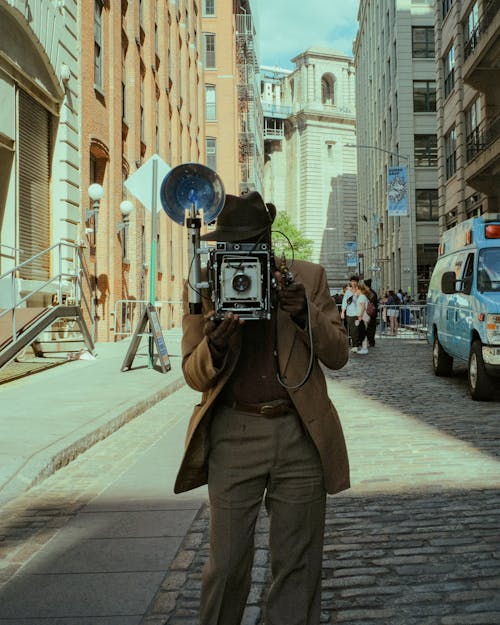 A man in a brown suit holding a camera on a city street