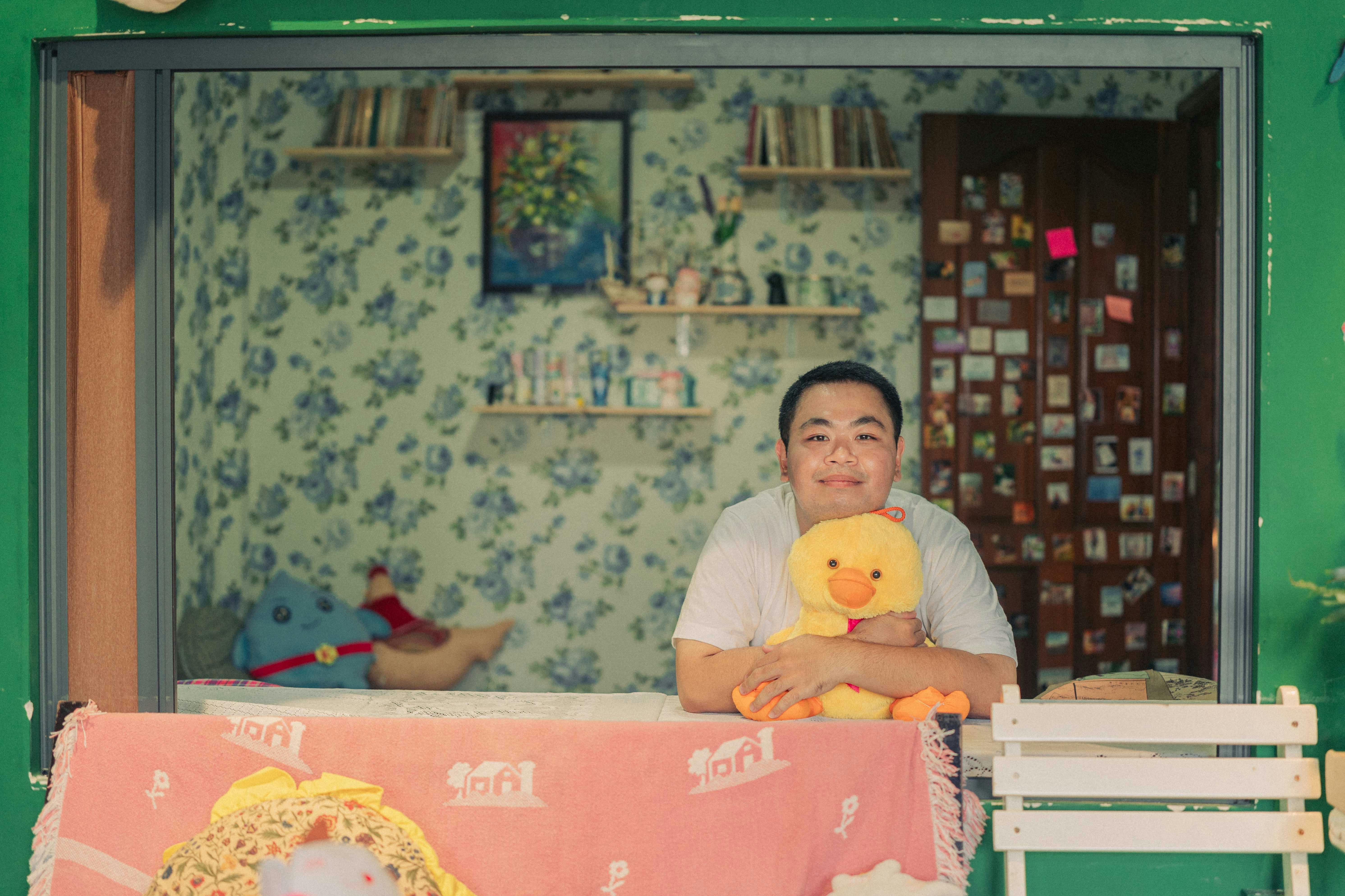 A man smiling while sitting with a plush toy in a cozy indoor setting.