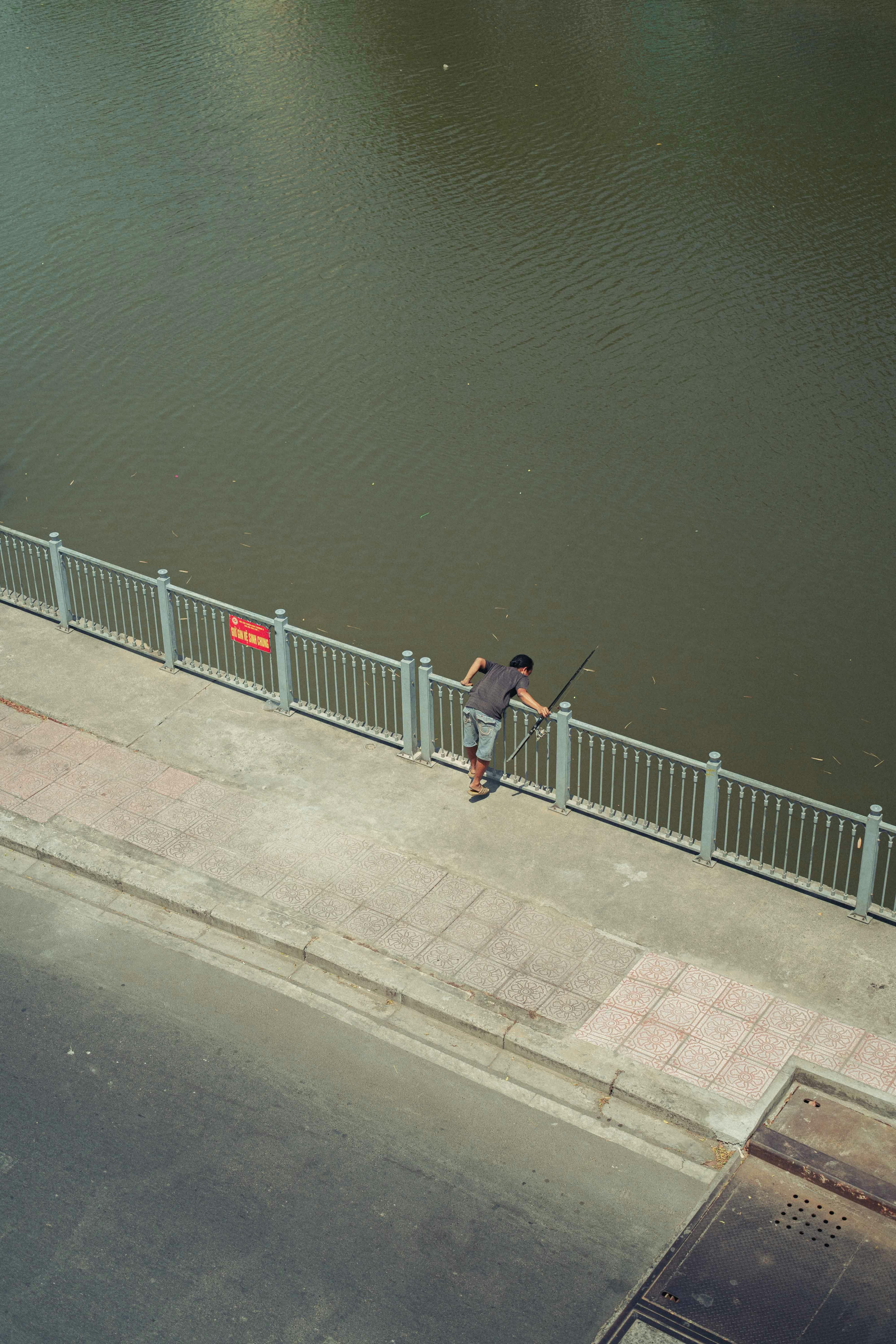 Aerial shot of a man fishing by a river in Ho Chi Minh City, Vietnam. Urban recreation scene.