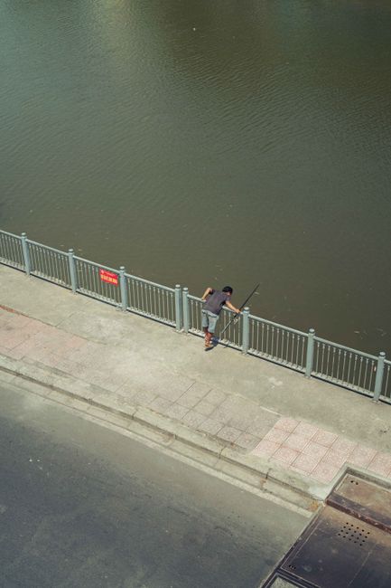 Aerial shot of a man fishing by a river in Ho Chi Minh City, Vietnam. Urban recreation scene.