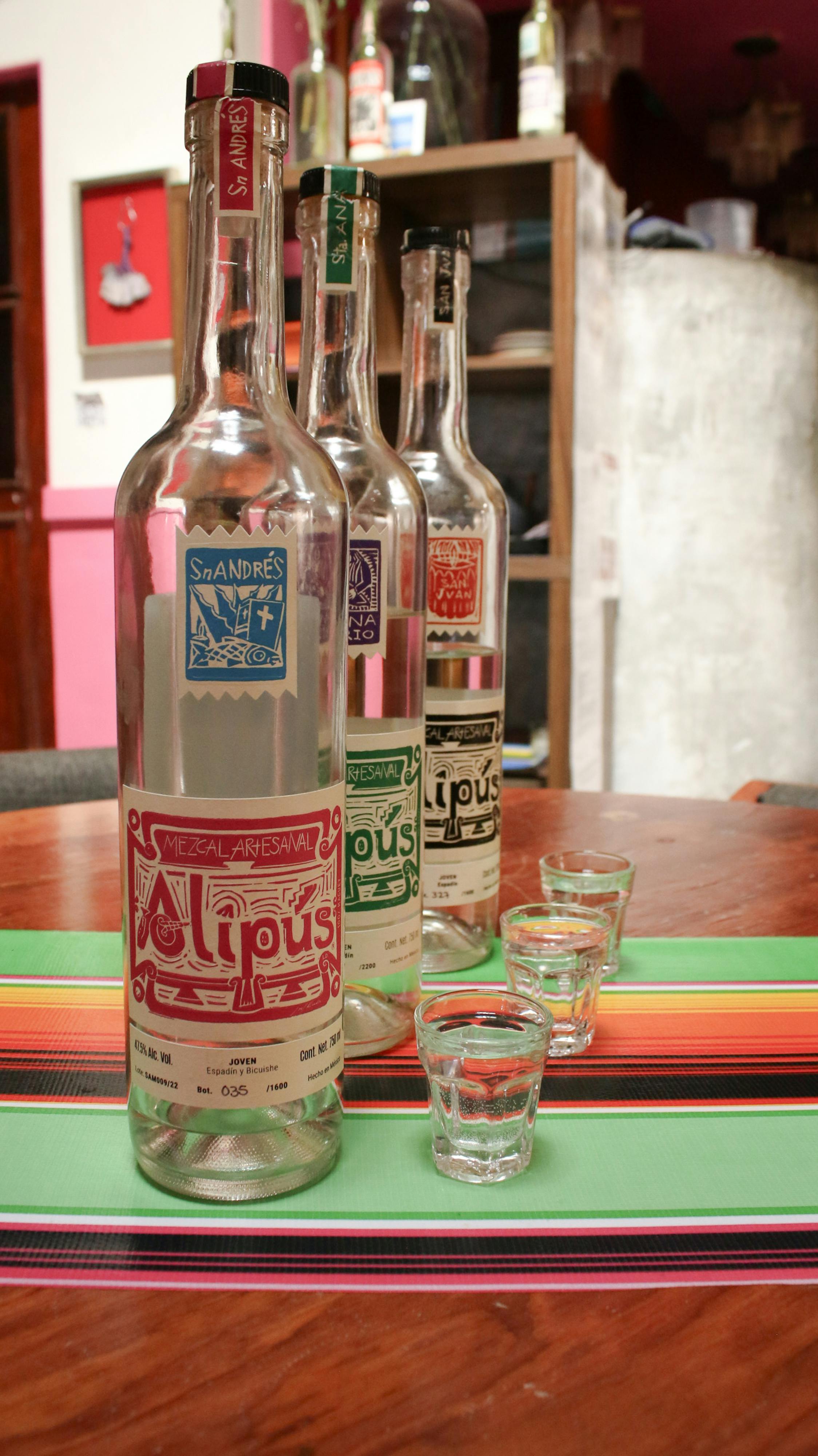 Vibrant mezcal bottles with shot glasses on a colorful table setting indoors.