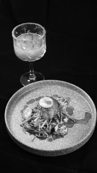 Black and white still life featuring a plated meal and cocktail glass on a dark background.