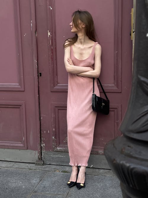 A woman in a pink dress leaning against a pink door