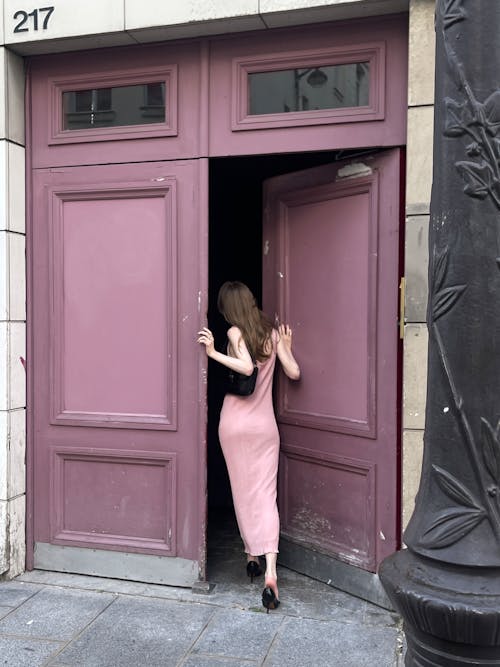 A woman in a pink dress is standing in front of a pink door