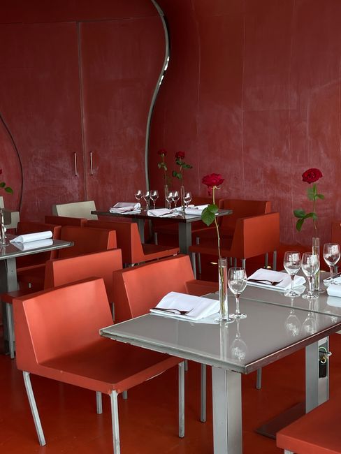 Elegant restaurant interior with red chairs and roses on tables, creating a romantic ambiance.
