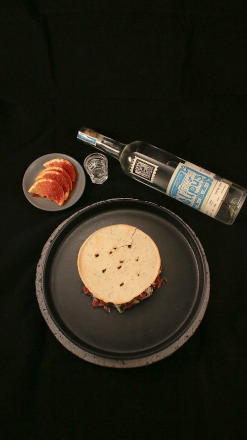 A black plate with a tortilla and a bottle of vodka