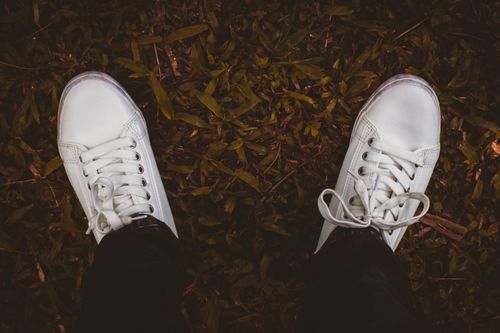 Free White sneakers on a leafy ground, showcasing casual outdoor fashion style. Stock Photo