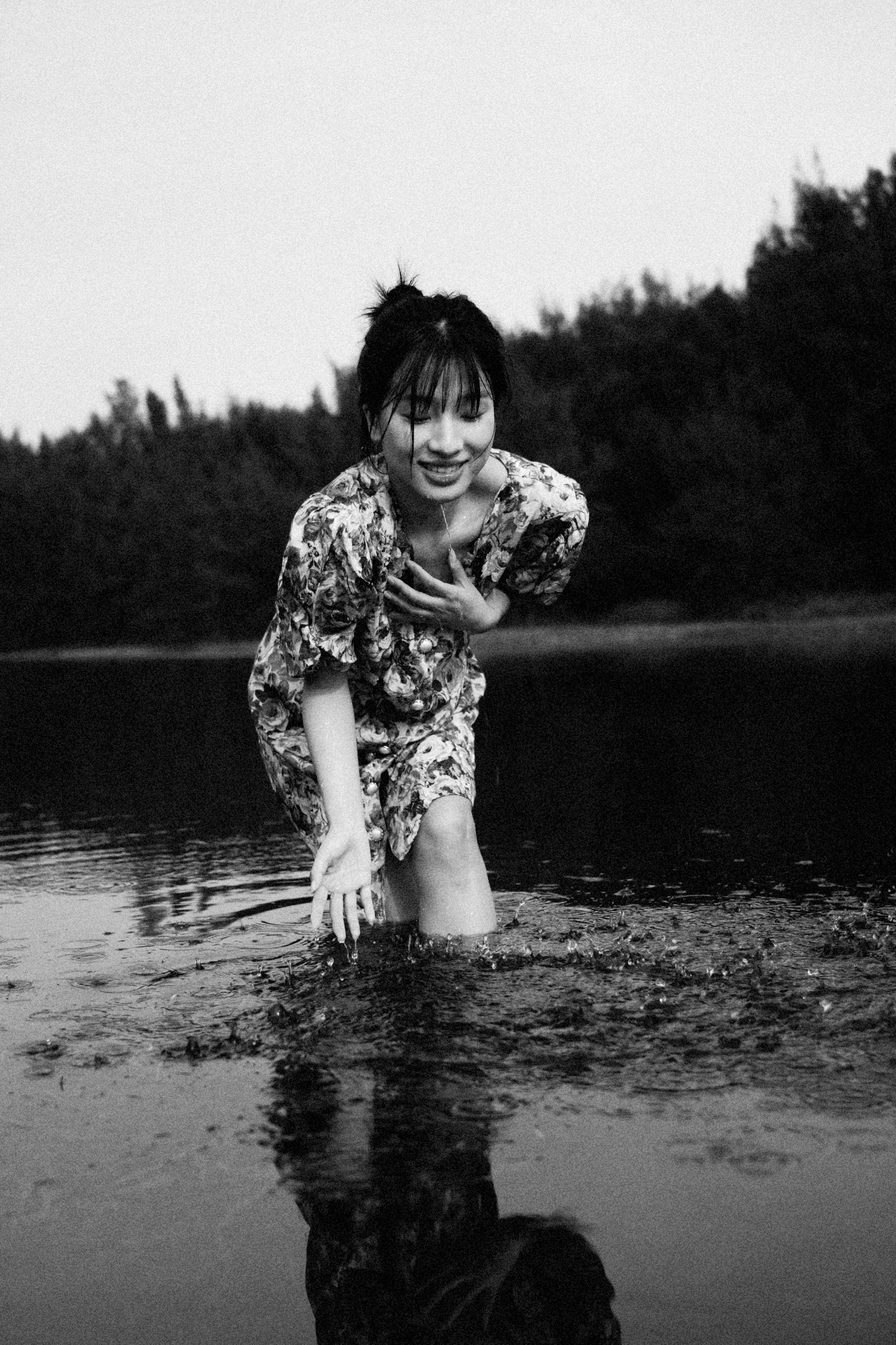 Black and white photo of an Asian woman laughing and playing in a lake.