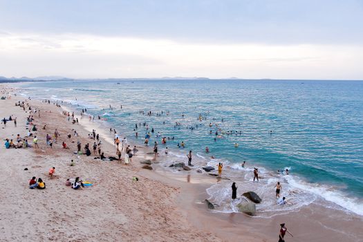 A lively beach scene with many people enjoying the ocean on a sunny day.