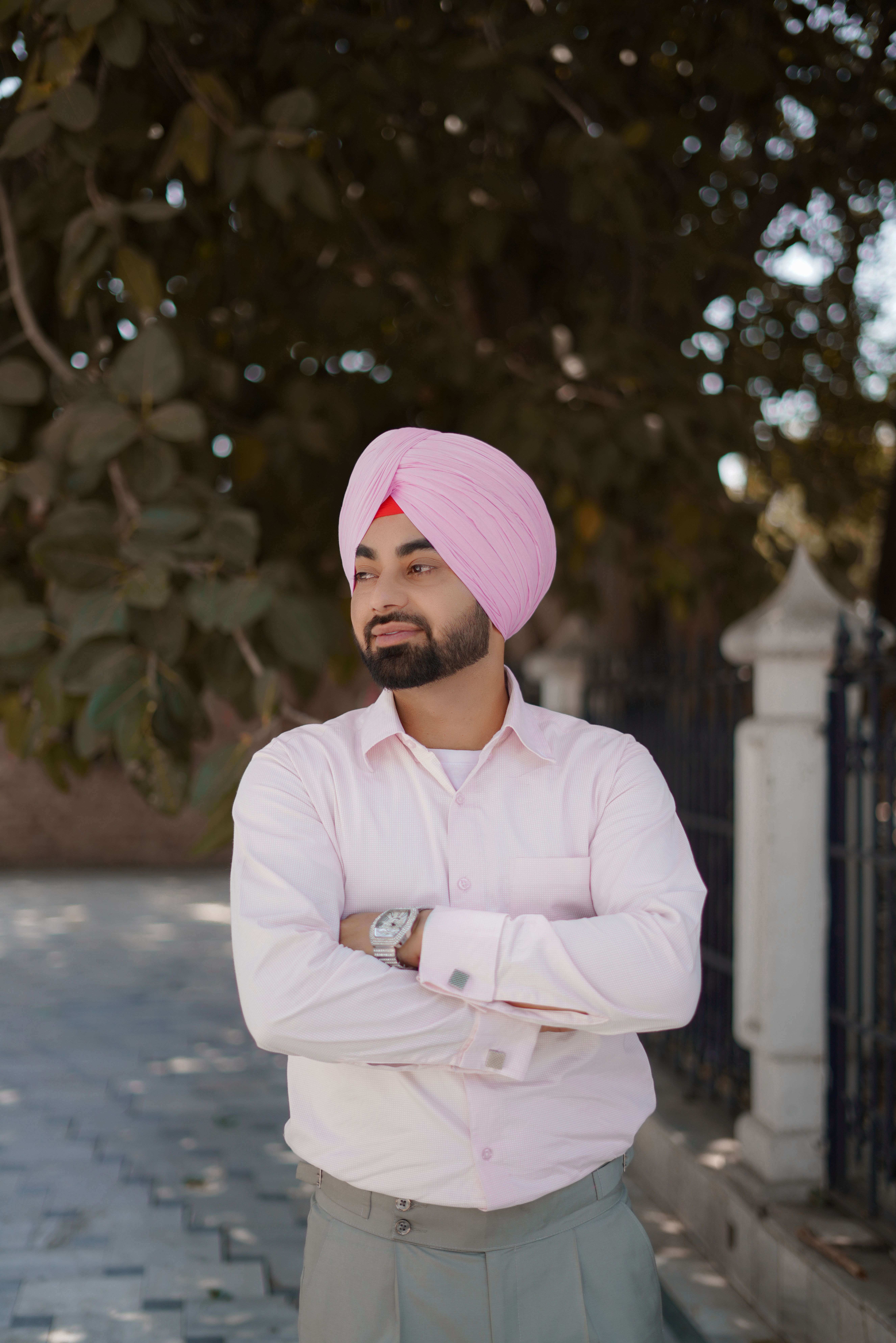Portrait of a stylish man in a pink turban and white shirt standing outdoors in Amritsar, India.