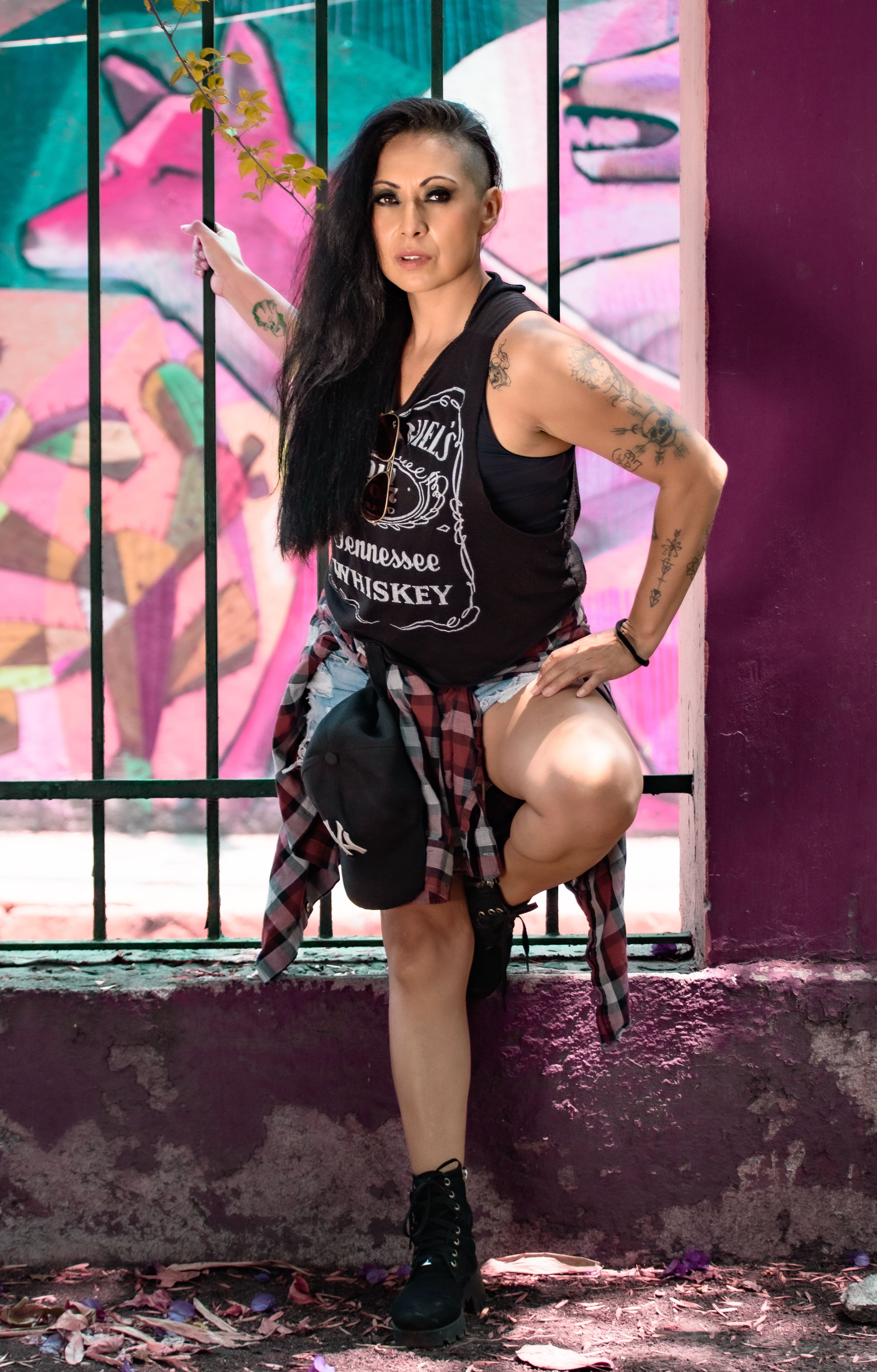 A fashionable woman in rock style clothing posing against a graffiti wall.