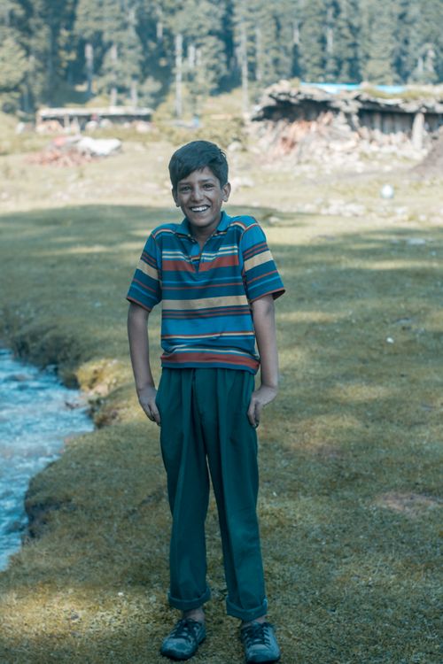 Free A cheerful boy stands smiling in a lush rural setting in Srinagar, India. Stock Photo