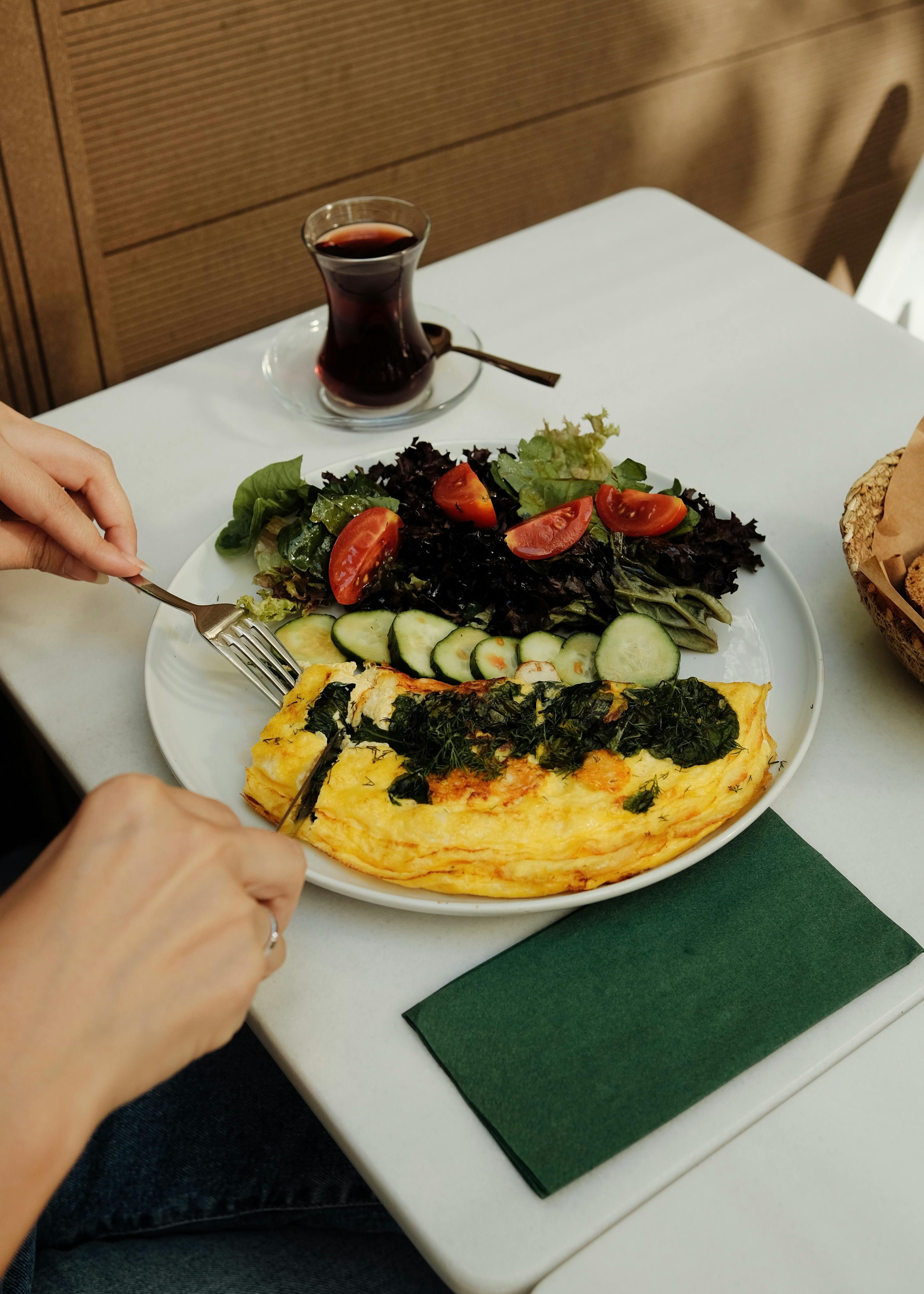 Person enjoying a nutritious meal with an omelette and fresh salad on a table.
