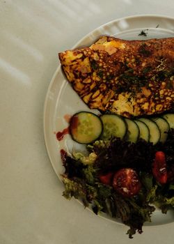 Top view of an omelette with cucumber slices and salad on a white plate, perfect for breakfast.
