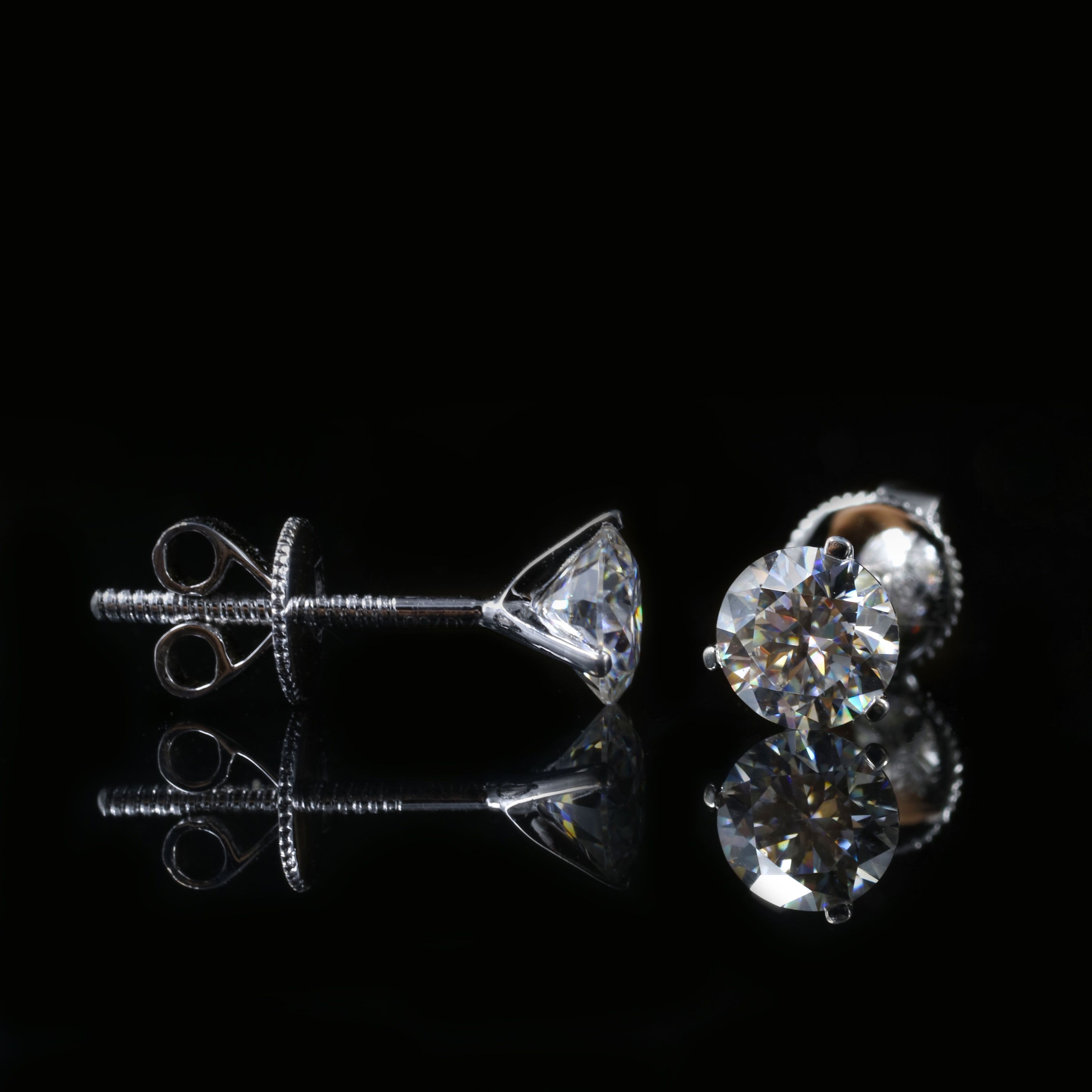 Close-up of elegant silver and diamond stud earrings against a black background, showcasing luxury and style.