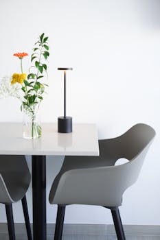 Elegant minimalist scene with a chair, lamp, and floral arrangement on a table.