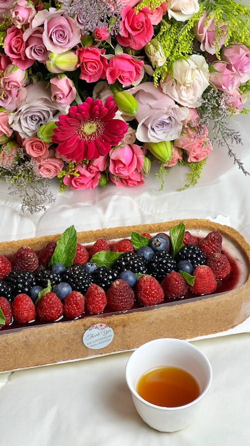 A tray with berries and flowers next to a cup of tea