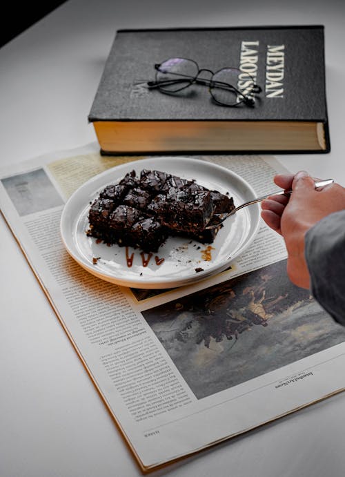 A person is eating a piece of chocolate cake on a newspaper