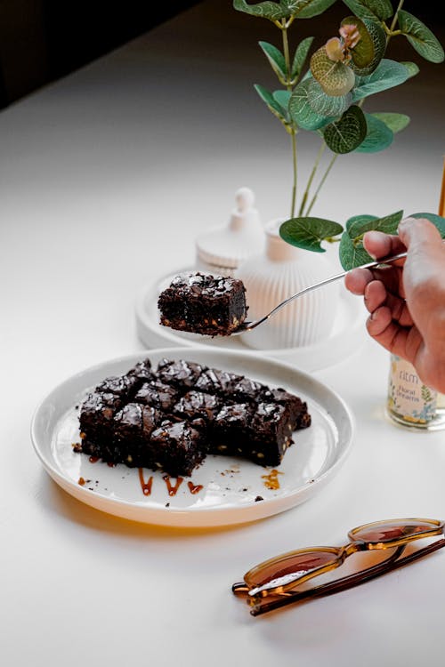 A person is holding a fork over a piece of chocolate cake