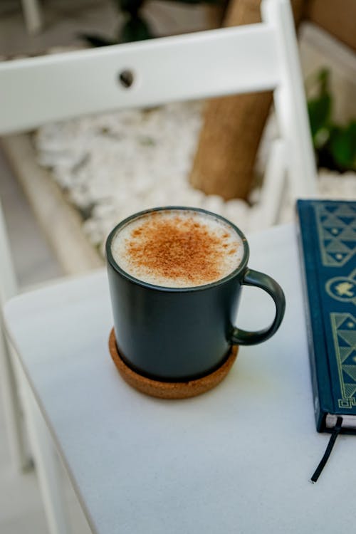 A cup of coffee sits on a table next to a book