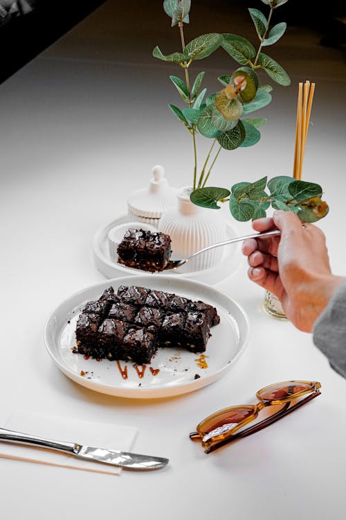 A person is holding a fork and knife over a plate of brownies