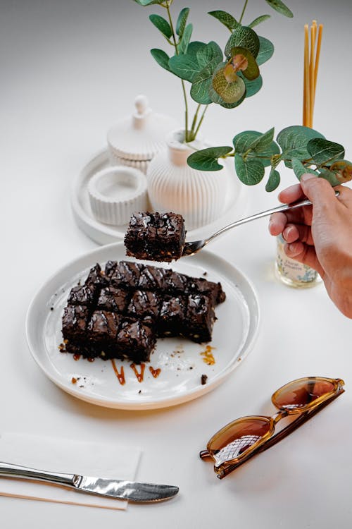 A person holding a fork and knife over a plate of brownies
