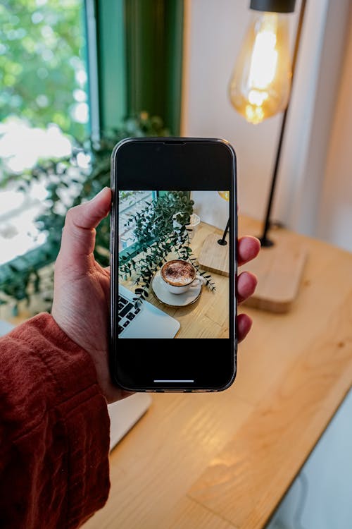 A person holding up their phone to take a picture of a coffee cup