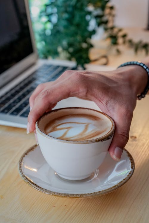 A person holding a cup of coffee with a laptop in the background