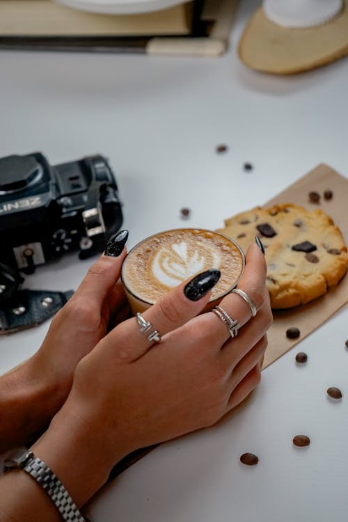 A person holding a coffee cup with a cookie and a camera