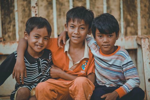 Free Three young boys sitting together and smiling, showcasing friendship and joy. Stock Photo