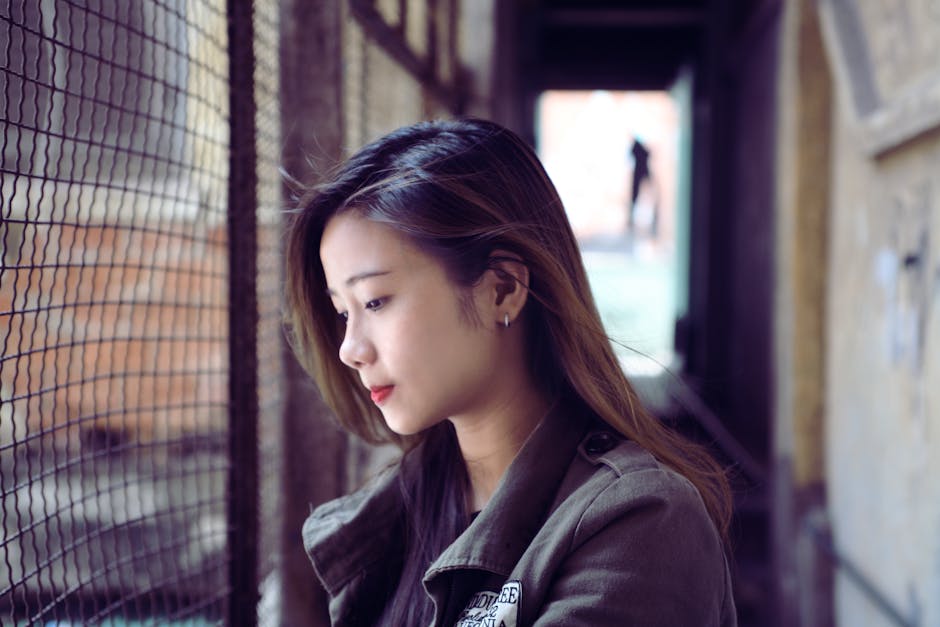 Portrait of a contemplative woman with red lips looking through a fence indoors.