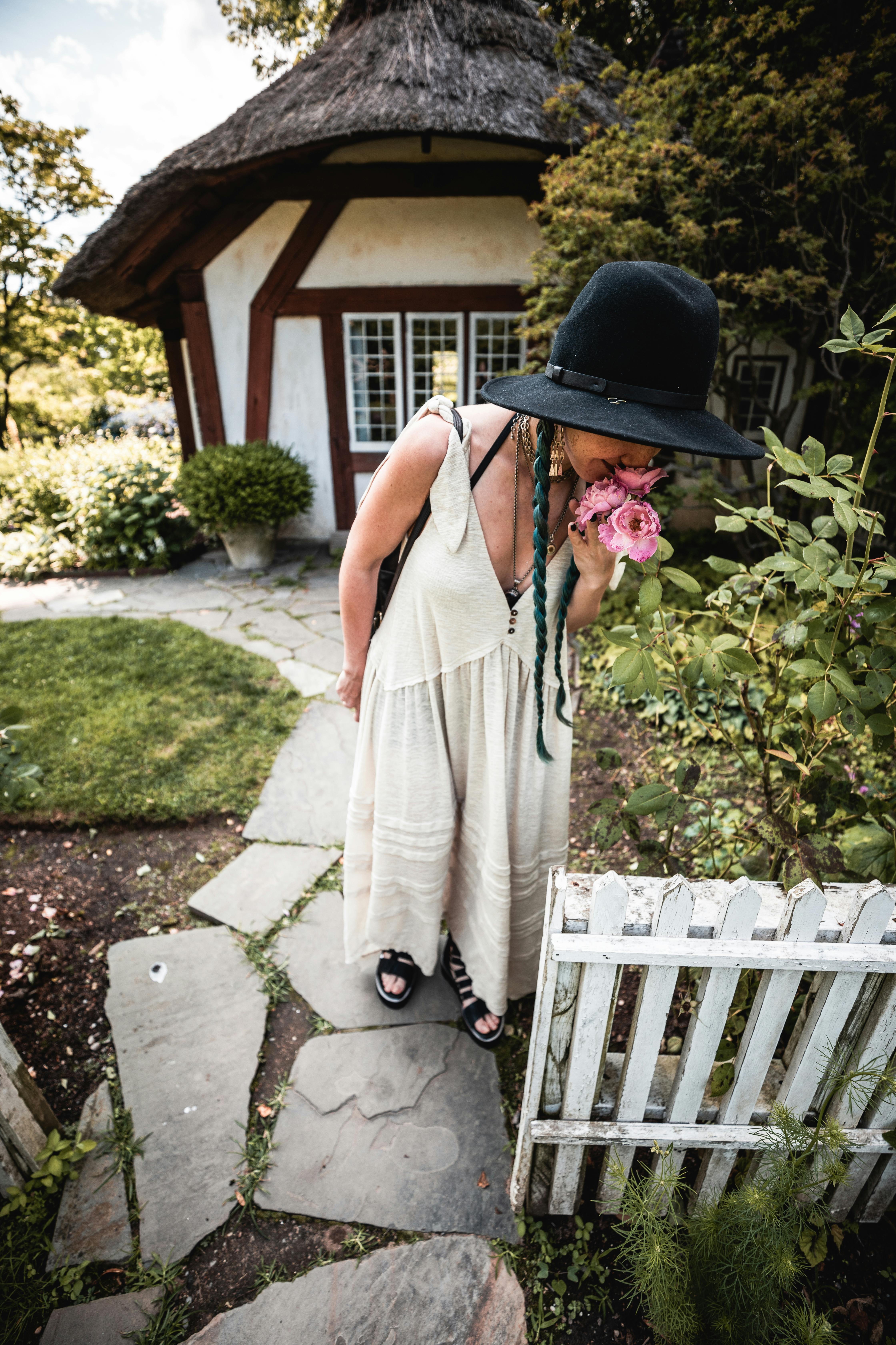 一位戴着帽子的女人在迷人的花园凉亭旁，享受着玫瑰的芬芳