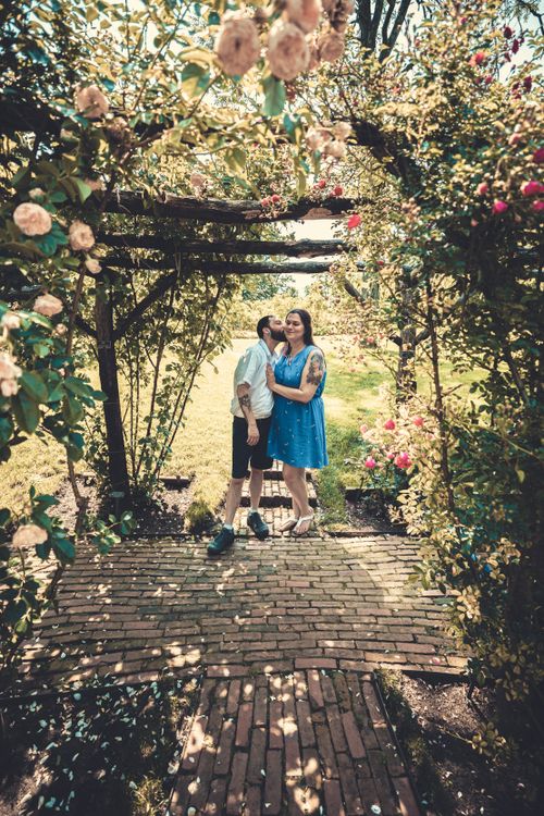 Free A couple stands embracing under a floral arch in a sunlit garden, symbolizing love and togetherness. Stock Photo