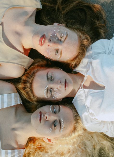 Three women with creative face art lying on the ground, captured from above.