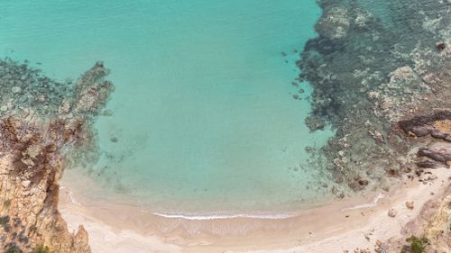 Free Stunning aerial view of a rocky ocean shore with clear turquoise water and sandy beach. Stock Photo
