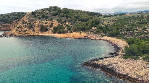 Free Scenic aerial view of a rocky seashore with clear turquoise waters and lush greenery. Stock Photo