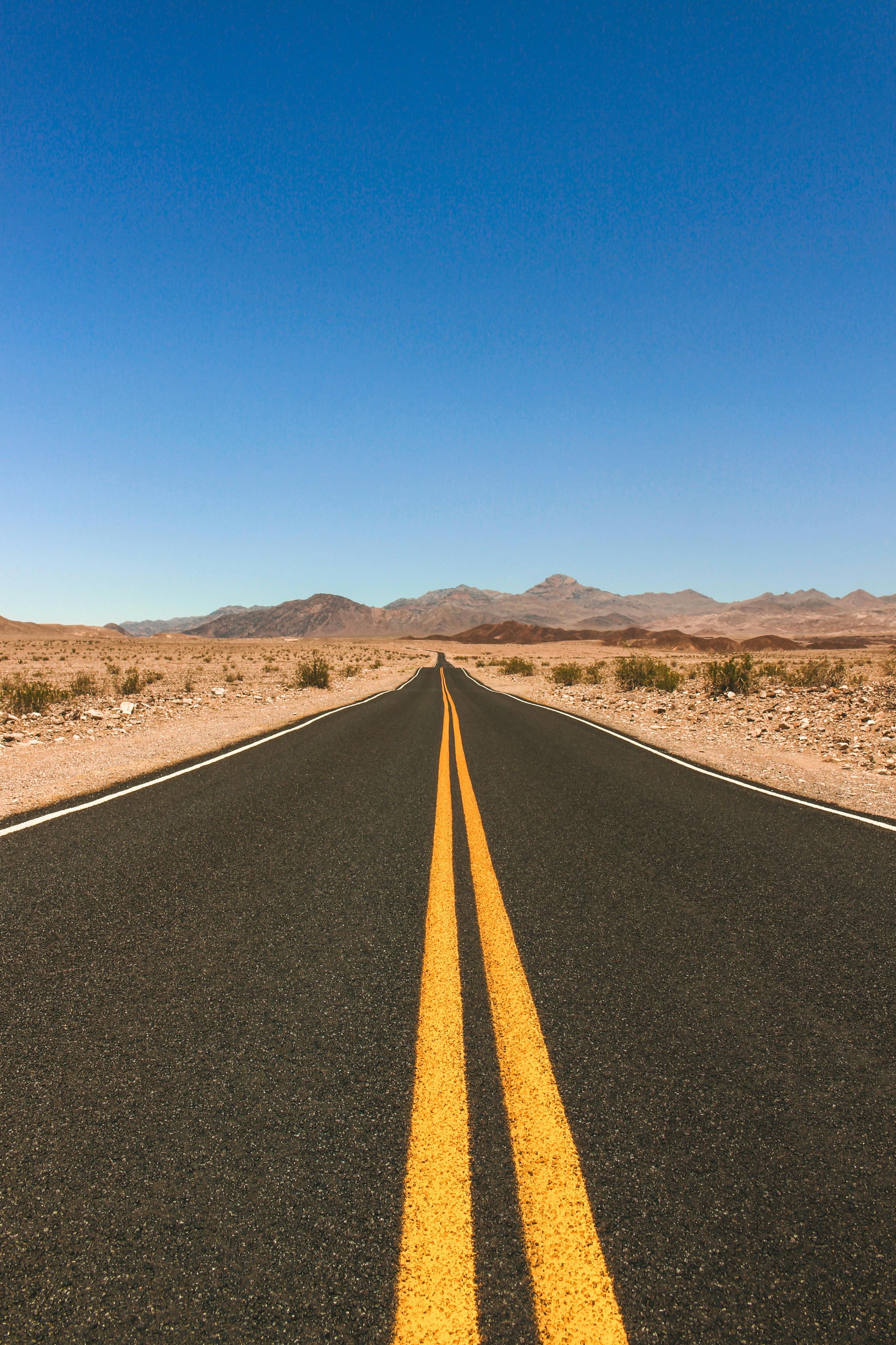 Long straight road in California desert under clear blue sky, ideal for travel themes.