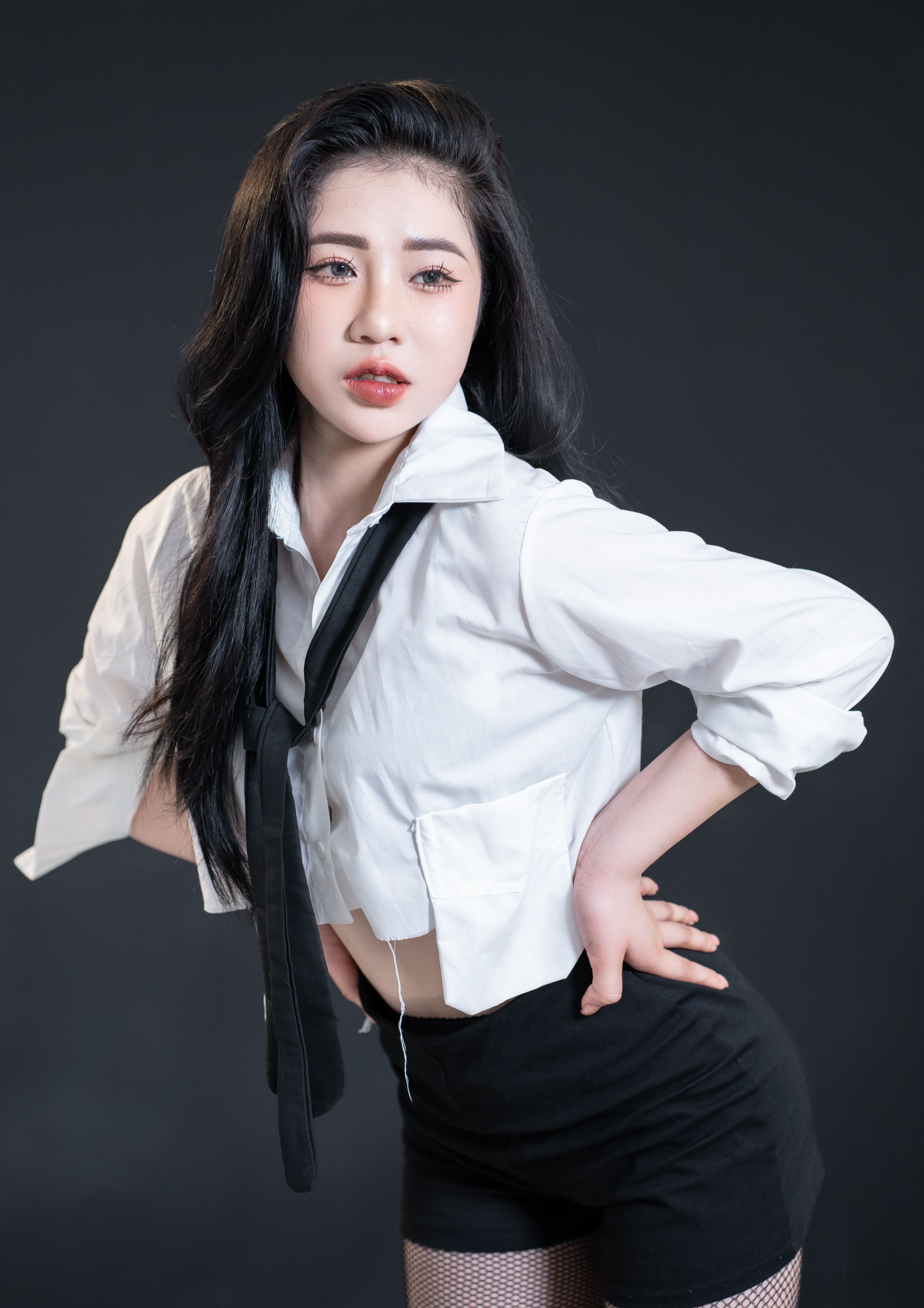 Stylish portrait of a young woman posing in a studio, dressed in modern fashion attire.