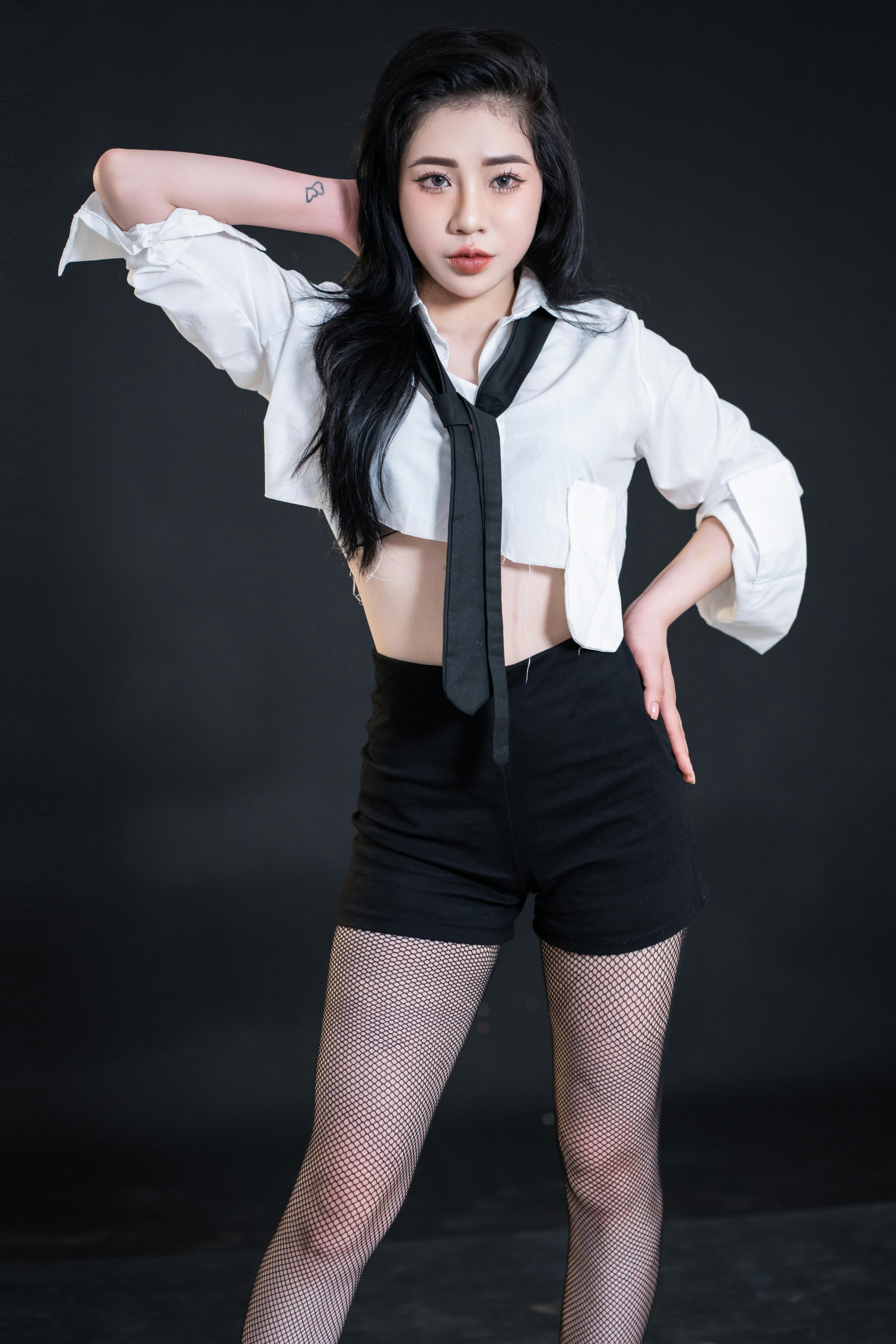 Asian woman confidently posing in a modern studio shoot wearing a stylish outfit with a black tie.