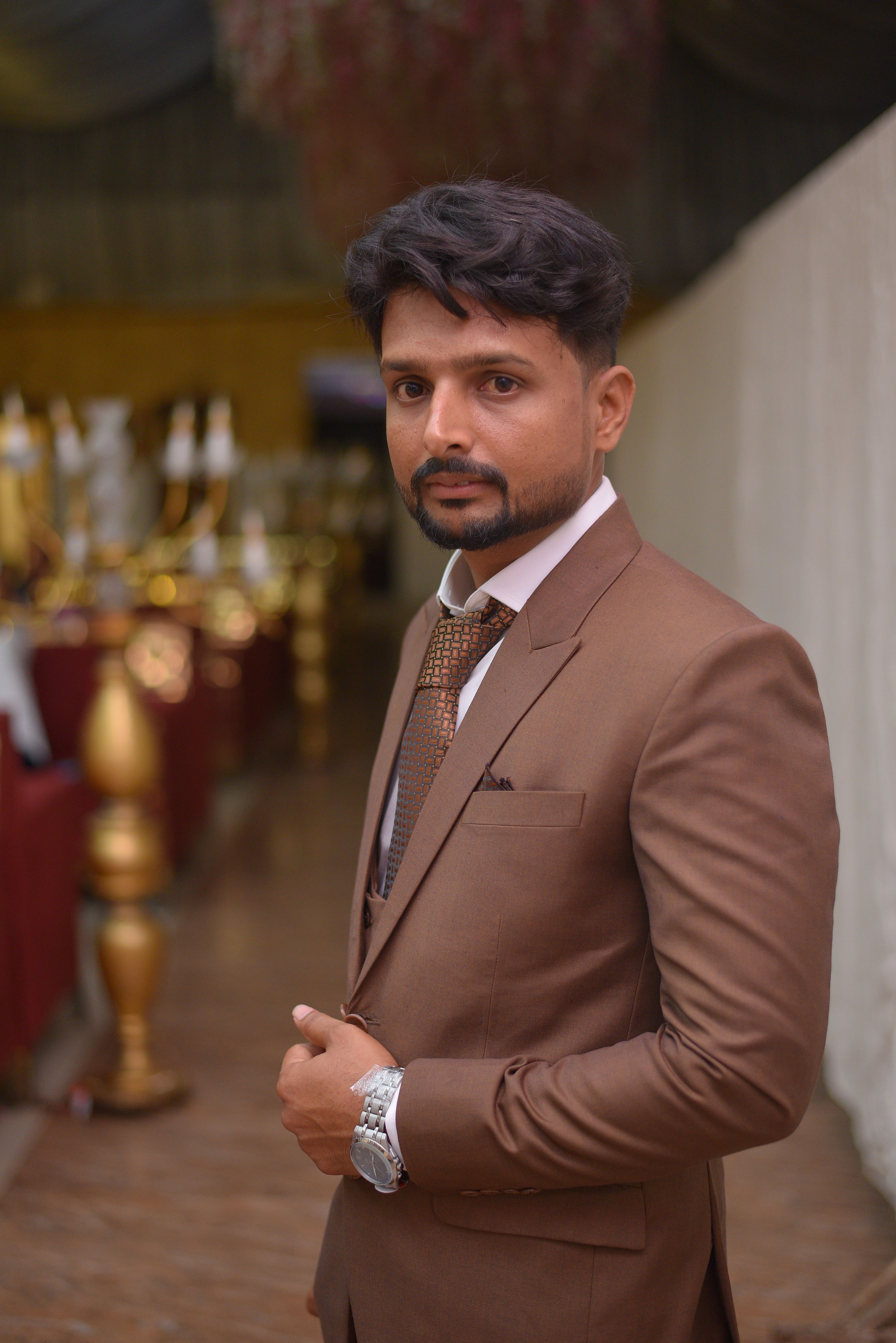 Elegant portrait of a man in a brown suit with a serious expression in an indoor setting.