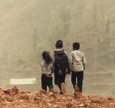Group of children walking on a hill in rural area, wearing backpacks.