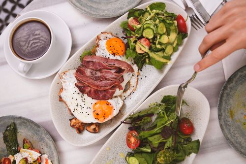 Free Top view of a brunch meal featuring fried eggs, bacon, fresh salad, and coffee. Stock Photo